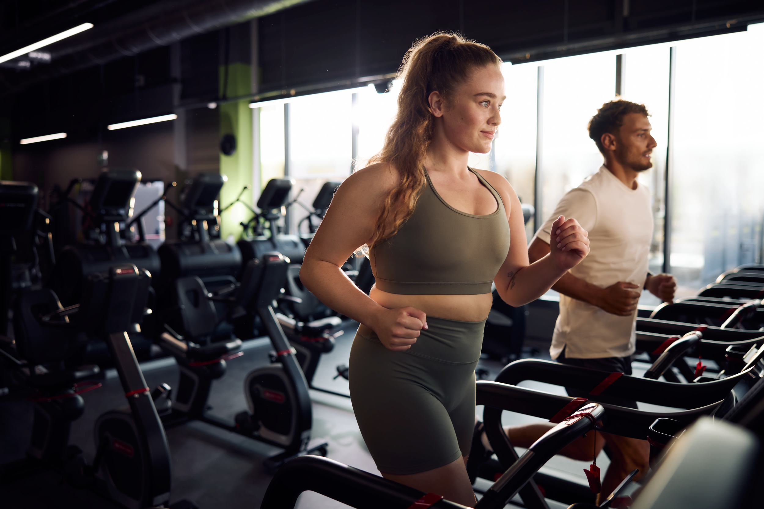 Kobieta i mężczyzna trenujący na bieżniach w Well Fitness