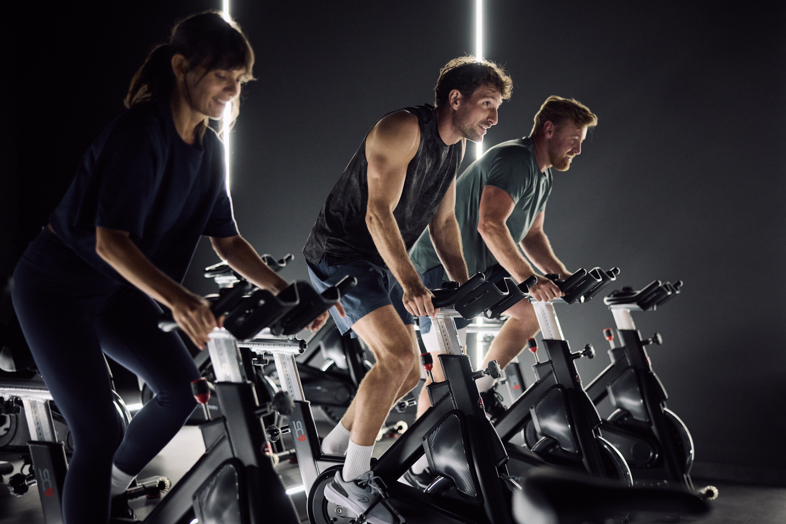 Grupa osób ćwiczących na rowerach stacjonarnych podczas zajęć Indoor Cycling w klubie fitness.
