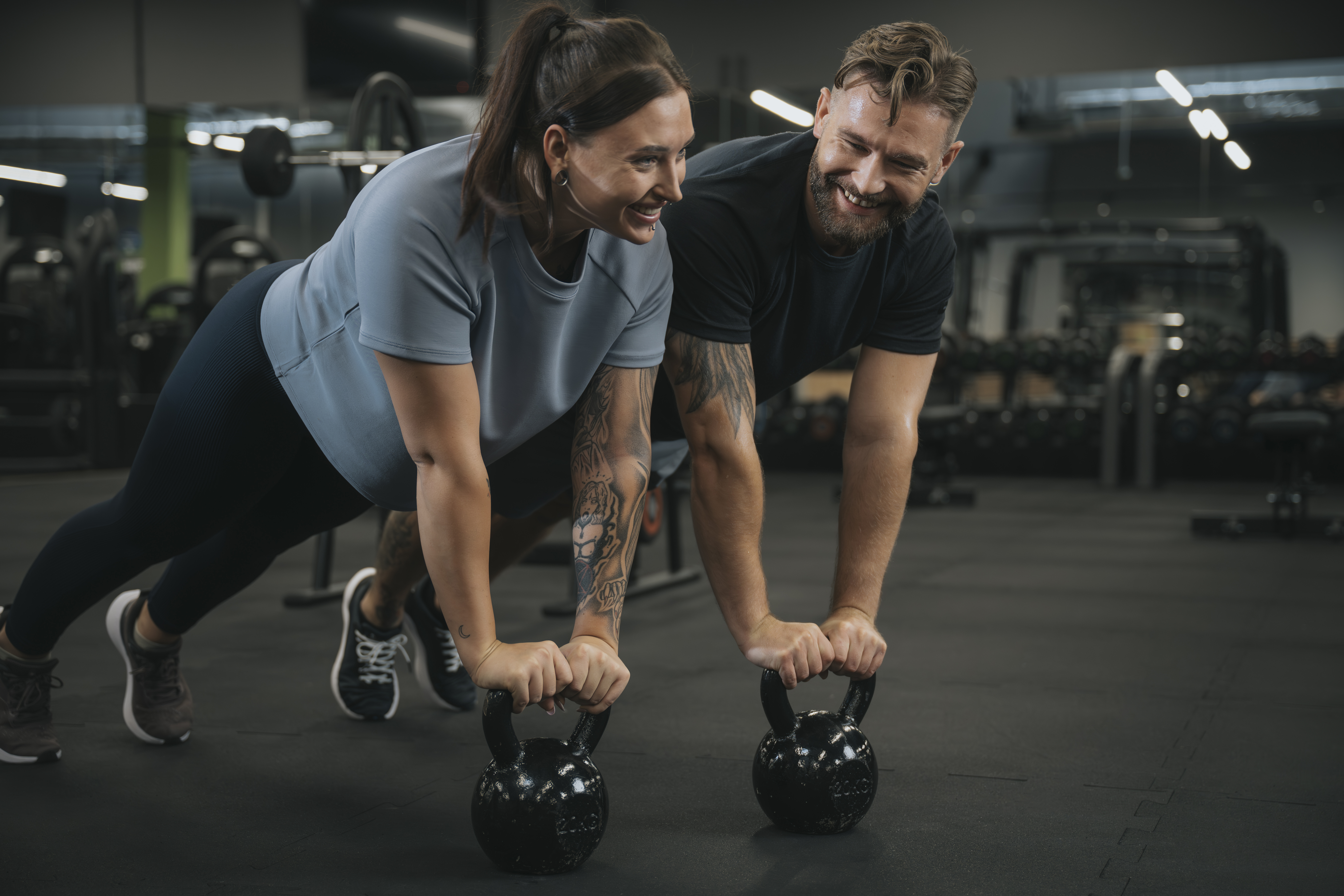 Kobieta i mężczyzna trenują mięśnie brzucha w podporze na kettlebellach podczas zajęć w klubie fitness.