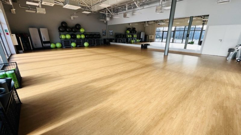 Duża sala do zajęć grupowych z lustrem oraz wyposażeniem do ćwiczeń fitness.