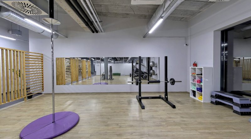 Sala fitness z mata, sztangami oraz lustrem.