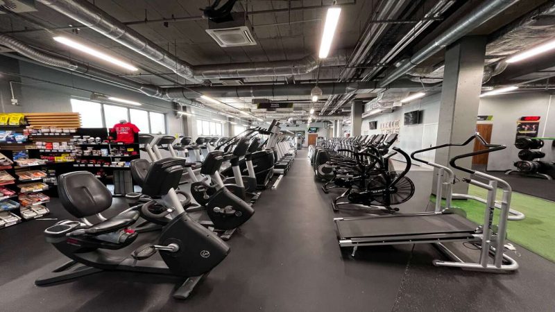Sala cardio, gdzie po dwóch stronach w rzędach stoją rowerki oraz bieżnie i orbitreki.
