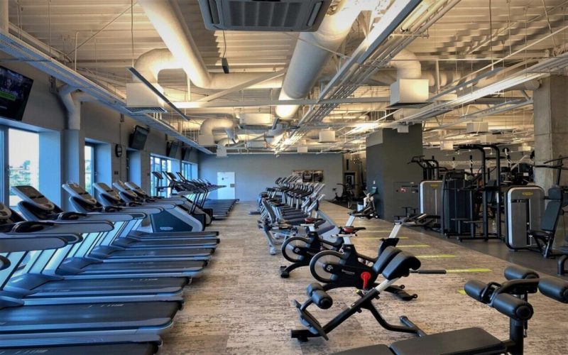 Sala ze strefą kardio. PO prawej stronie stoją rowerki, po lewej pod oknem bieżnie.