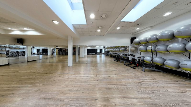 Sala fitness do ćwiczeń siłowych. na ścianach wisza lustra a przy nich leżą akcesoria do ćwiczeń.