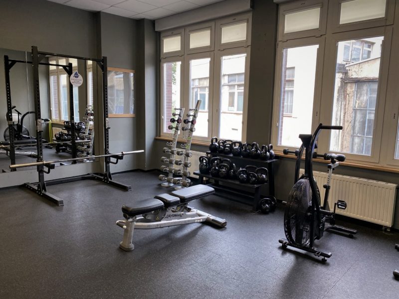 Pod oknem stoi stojak na kettlebells a obok niego ławeczki.