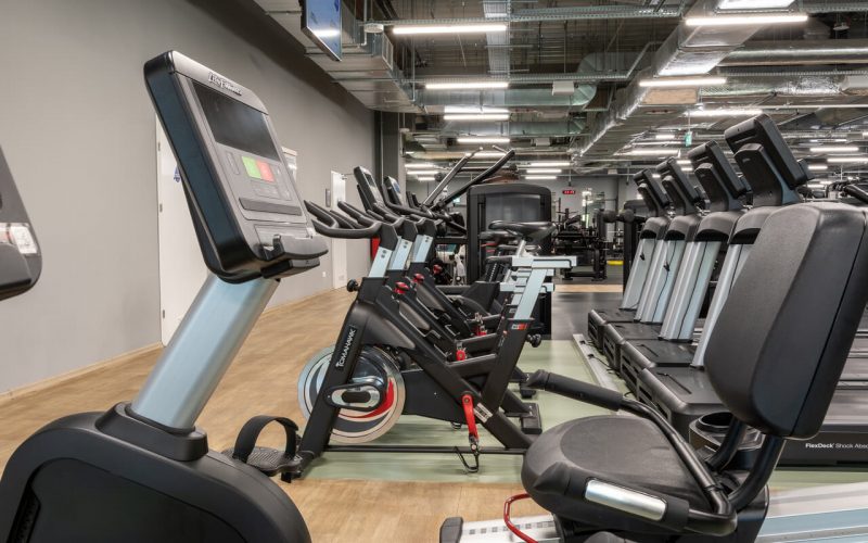 Ciąg rowerków do spinningu. Po prawej stronie rząd bieżni.