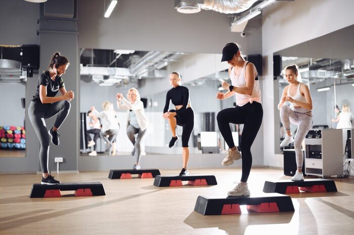 Kobiety podczas zajęć STEP na sali fitness, taneczne ruchy z wykorzystaniem stepów