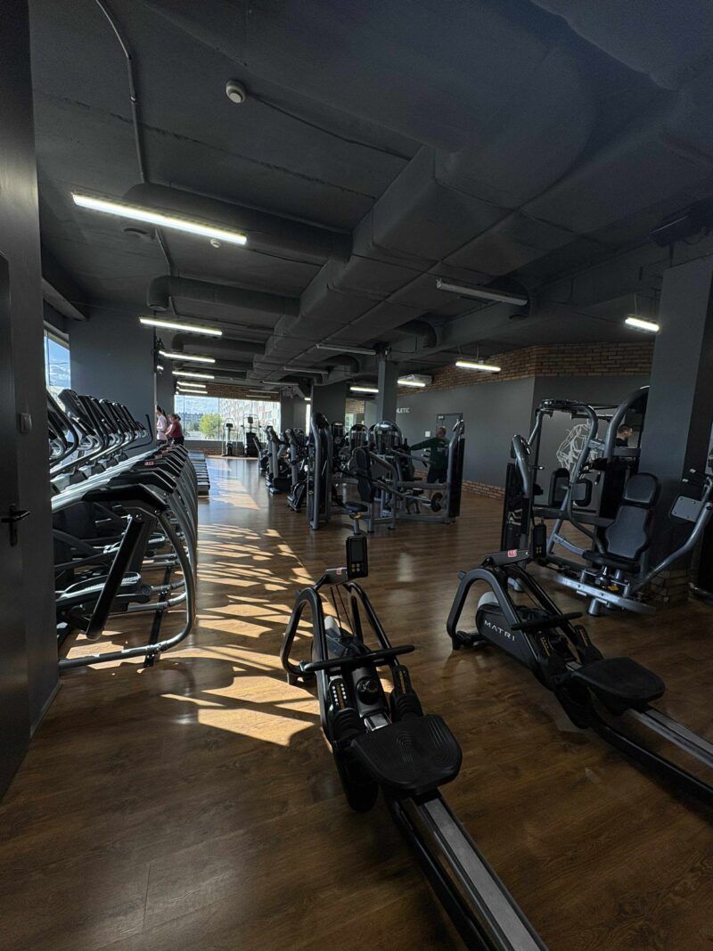 Orbitreki i schody treningowe w strefie cardio klubu fitness.