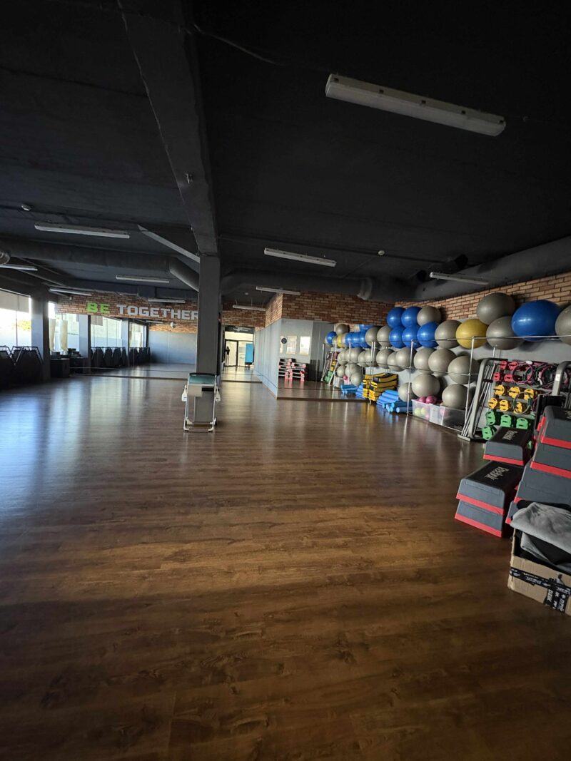 Sala fitness z lustrami i uczestnikami zajęć grupowych.