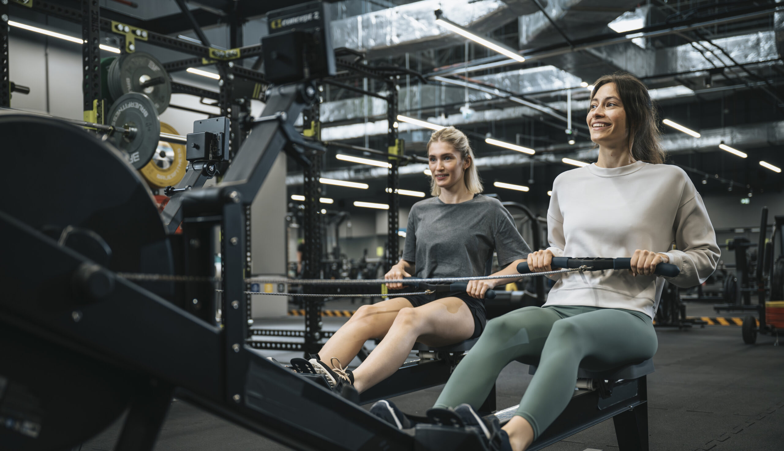 dwie kobiety ćwiczące przy pomocy wioślarza w well fitness
