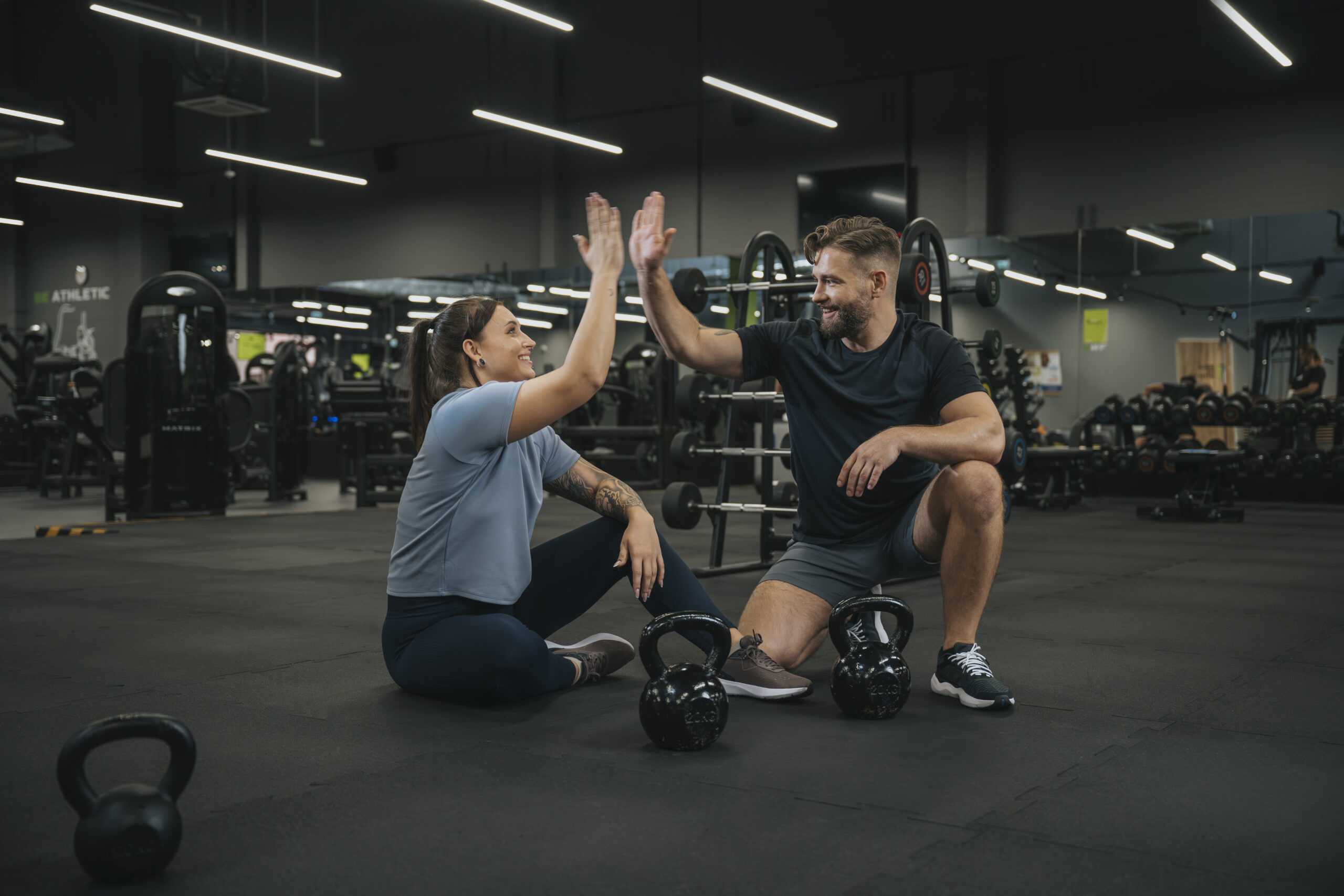 Trener i uczestniczka zajęć w siłowni przybijający piątkę po treningu z kettlebellami