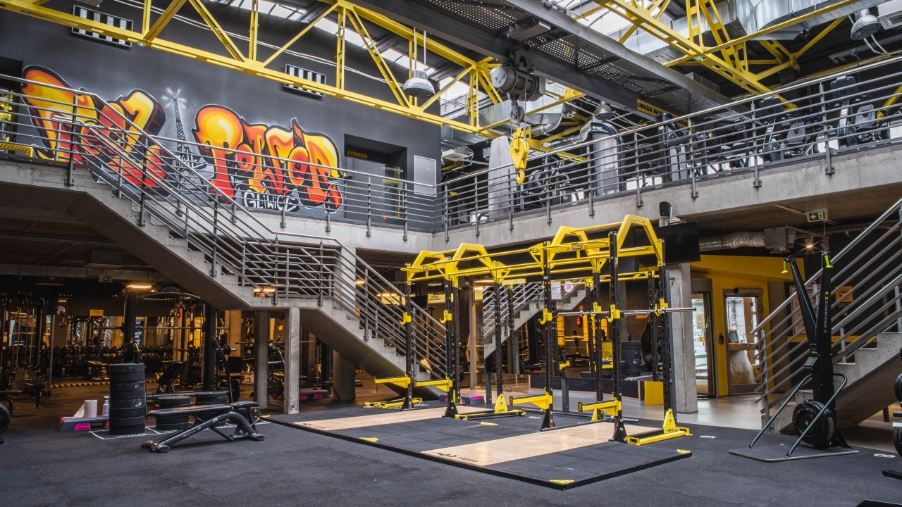 Przestronne, dwupoziomowe wnętrze siłowni o charakterze industrialnym. Na ścianie duże graffiti z napisem „POWER”. W centralnym punkcie klatki do przysiadów i pomosty ciężarowe. Widoczne schody prowadzące na antresolę.